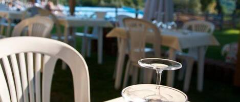 A table set with wine glasses and cutlery, under a tent with a view of a pool and greenery.