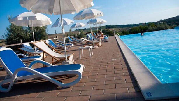 A poolside area with lounge chairs and umbrellas, a clear blue pool, and a brick pathway.