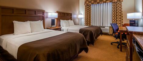 A hotel room with two beds, a desk, a chair, and a desk lamp.