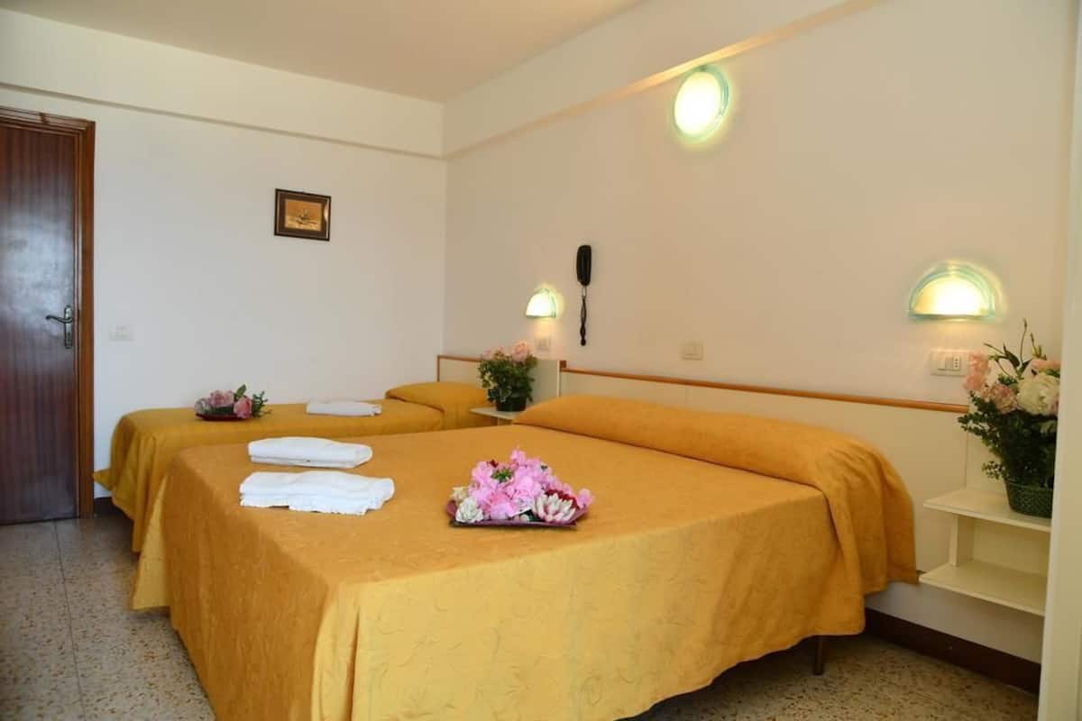 A hotel room with two beds, each with a yellow bedspread and white towels. There are wall-mounted light fixtures and a telephone on the wall.