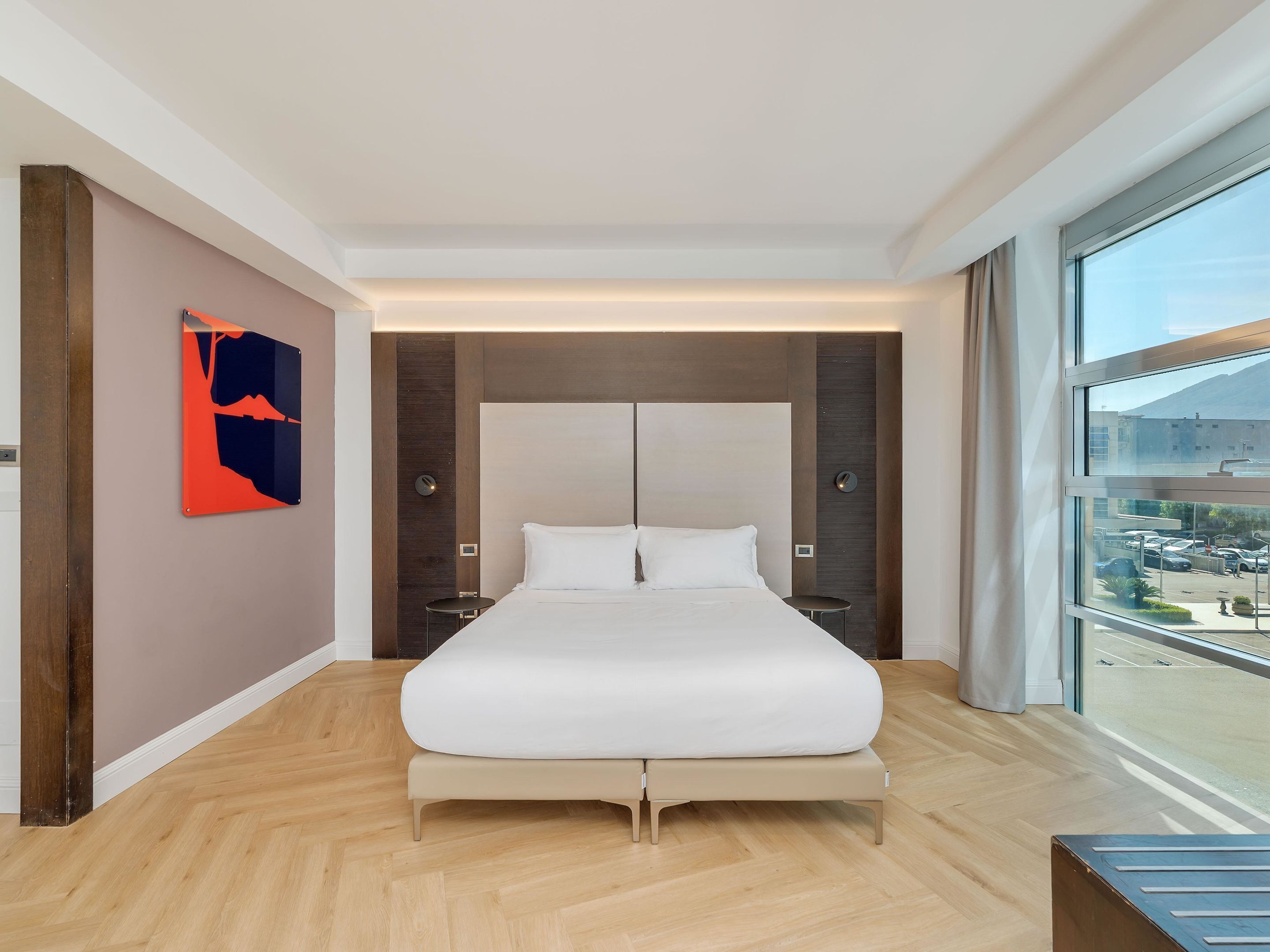Una habitación de hotel moderna con una cama grande, vistas a la ciudad y suelo de madera.