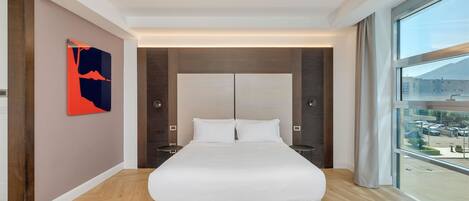 Una habitación de hotel moderna con una cama grande, vistas a la ciudad y suelo de madera.