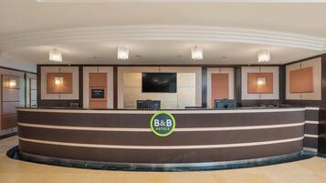 Un comptoir d’accueil orné du logo « B&B Hotels », un téléviseur à écran plat et un espace de réception au design moderne.
