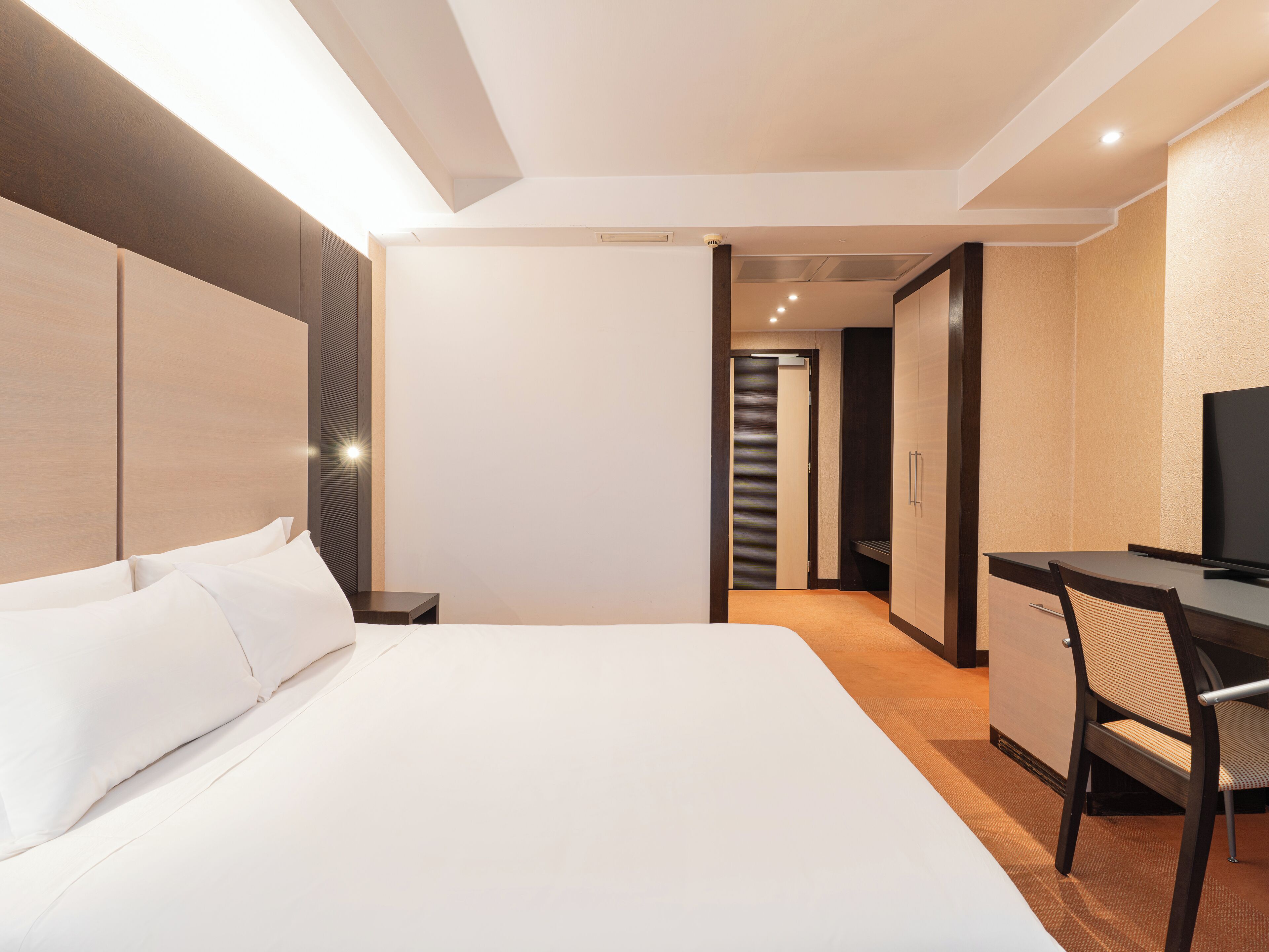 Habitación de hotel con una cama grande, un escritorio con silla, televisión y armario.