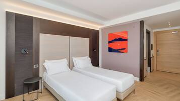 Una habitación de hotel moderna con dos camas, una mesita pequeña, una obra de arte colgada en la pared y una puerta de madera.