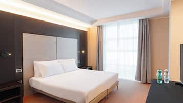 Habitación de hotel moderna con una cama grande, una mesita de noche, un televisor de pantalla plana y un ventanal con cortinas.