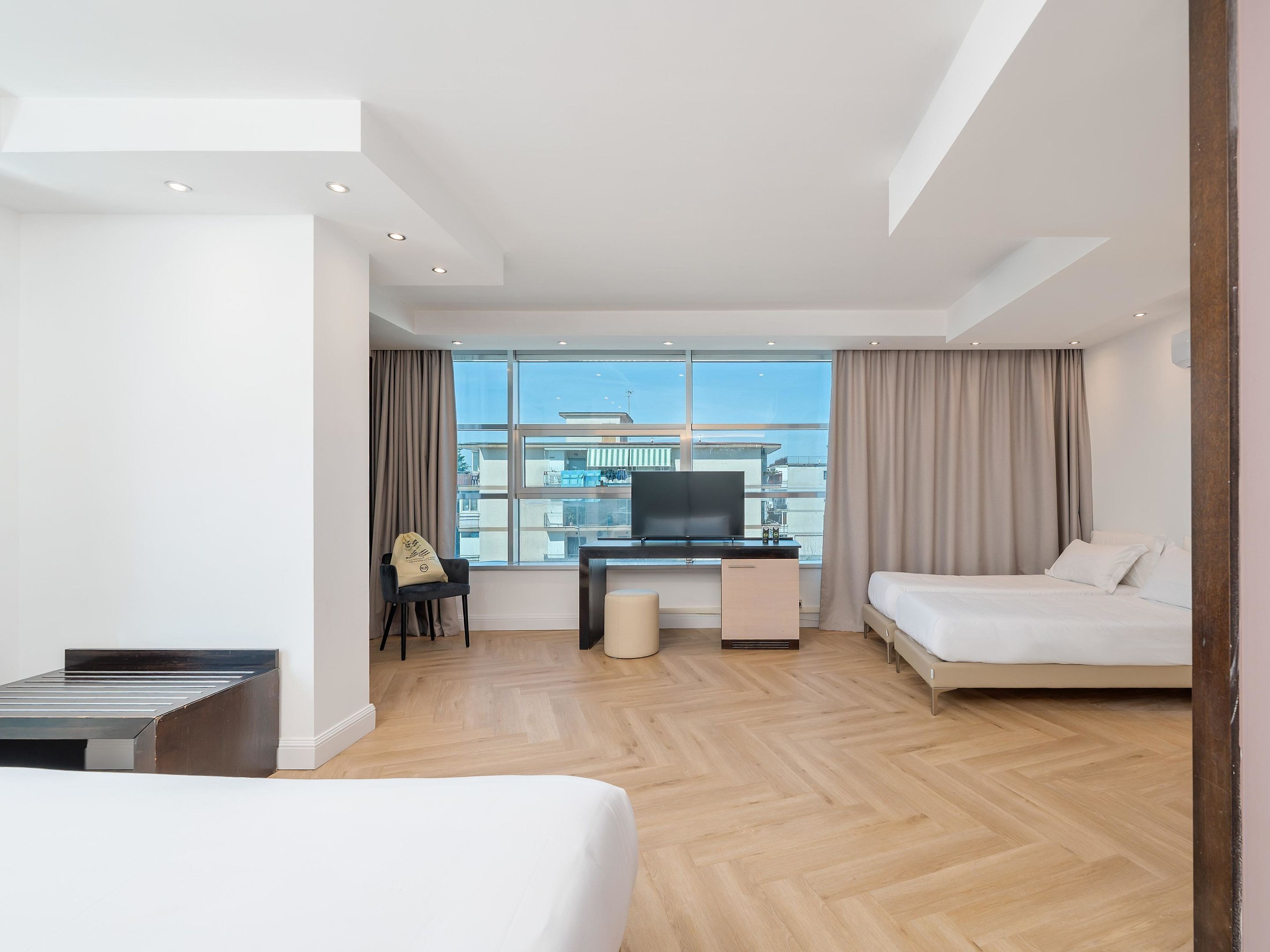 Habitación de hotel moderna con cama, escritorio con televisor, silla y vistas de la ciudad a través de amplios ventanales.