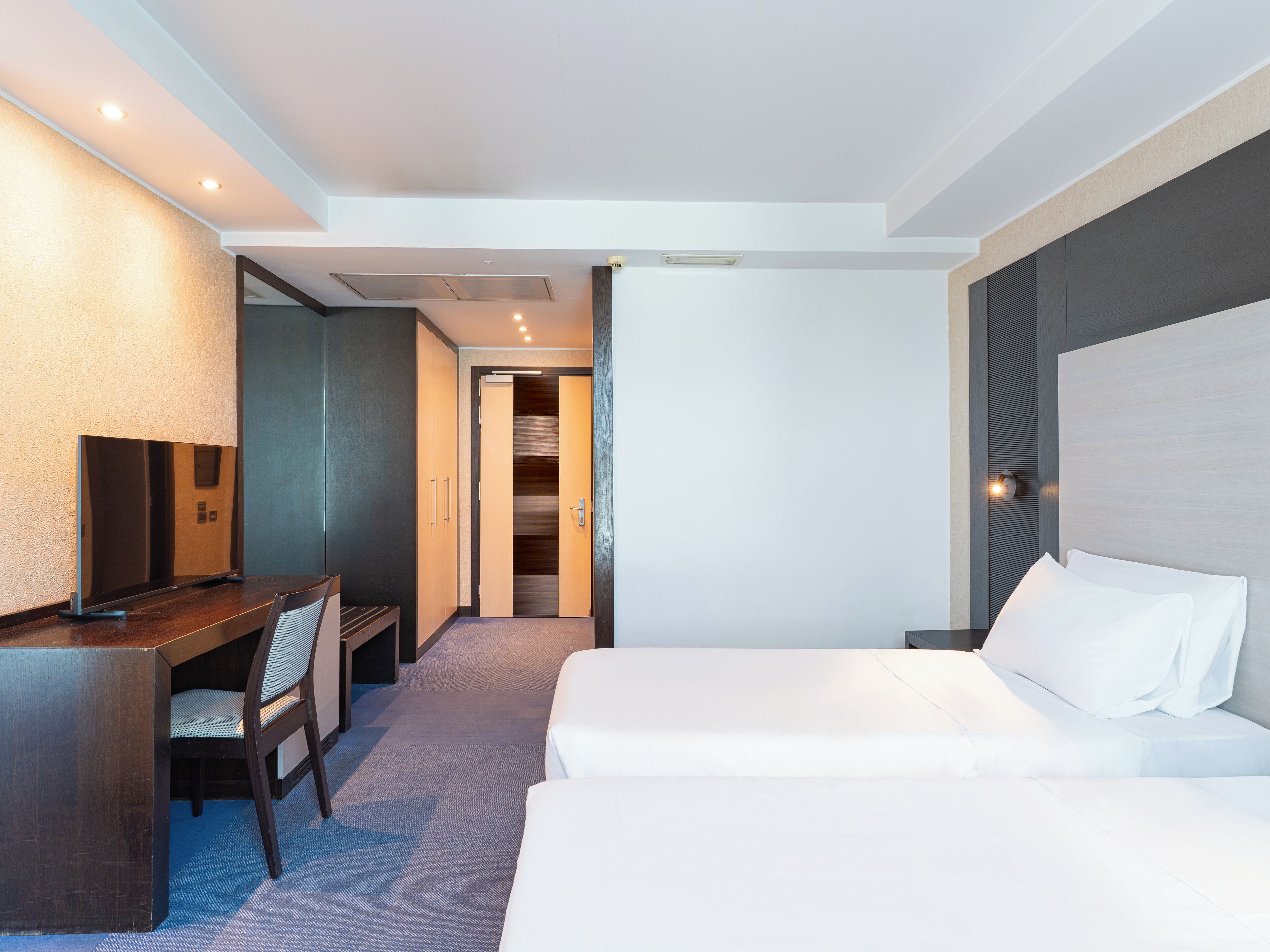 A hotel room with a desk, chair, and two beds.