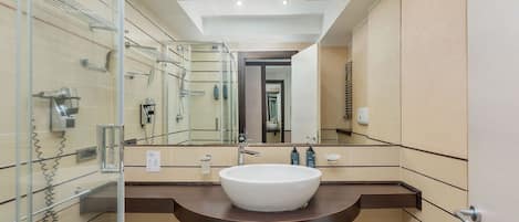 Uma casa de banho moderna com um espelho grande, uma pia branca e um cabine de duche em vidro.