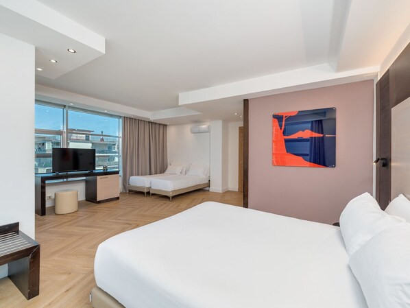A modern hotel room with a large bed, a desk with a TV, a small seating area, and a large window offering a city view. - B&B Hotel Napoli San Mauro (Casalnuovo di Napoli)