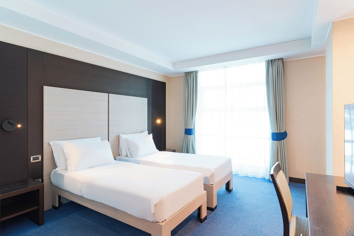 A hotel room with two beds, a desk, and a TV.