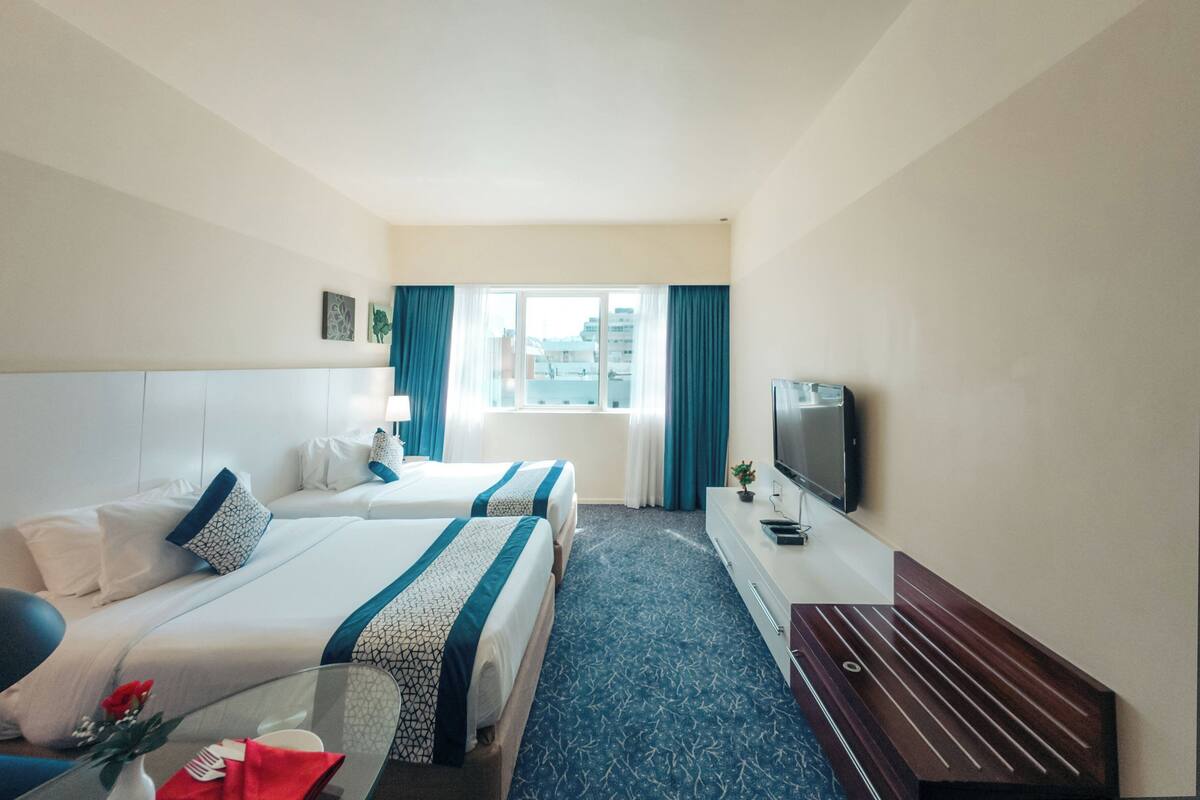 Une chambre d’hôtel avec deux lits, une télévision et une fenêtre avec des rideaux.