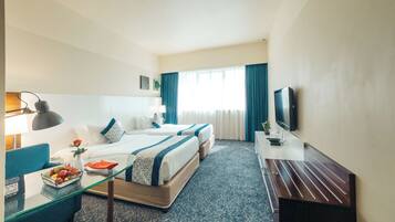 A hotel room with two beds, a desk, a TV, and a glass coffee table with fruit.
