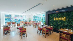 Un restaurant avec des tables et des chaises en bois, de grandes fenêtres et un mur végétal sur lequel le mot « food » est illuminé.