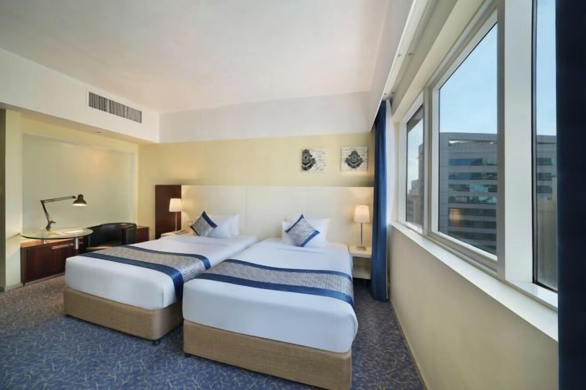 Habitación de hotel con dos camas, un escritorio, una lámpara y un ventanal grande.