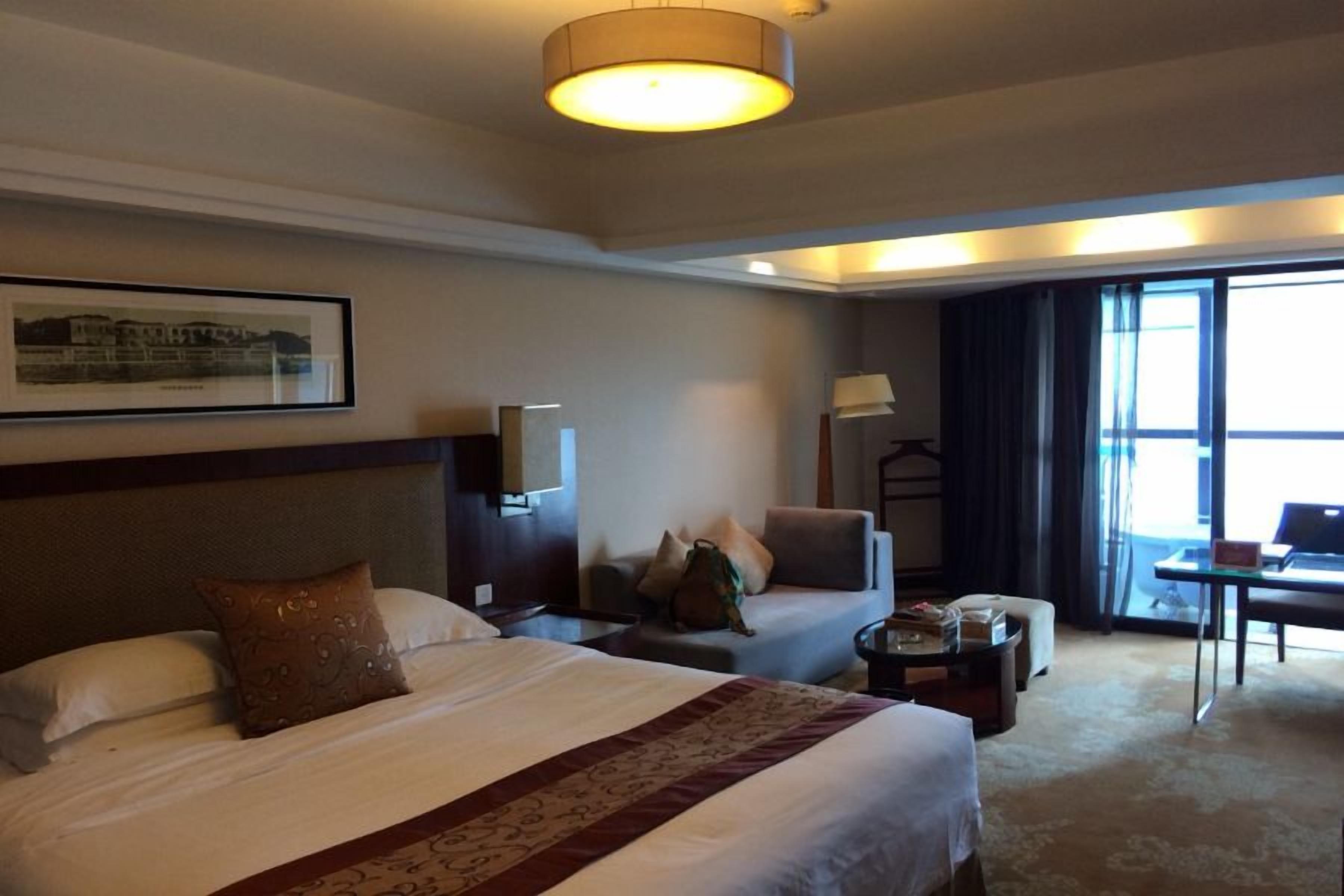 A hotel room with a large bed, a desk, a chair, and a window with curtains.