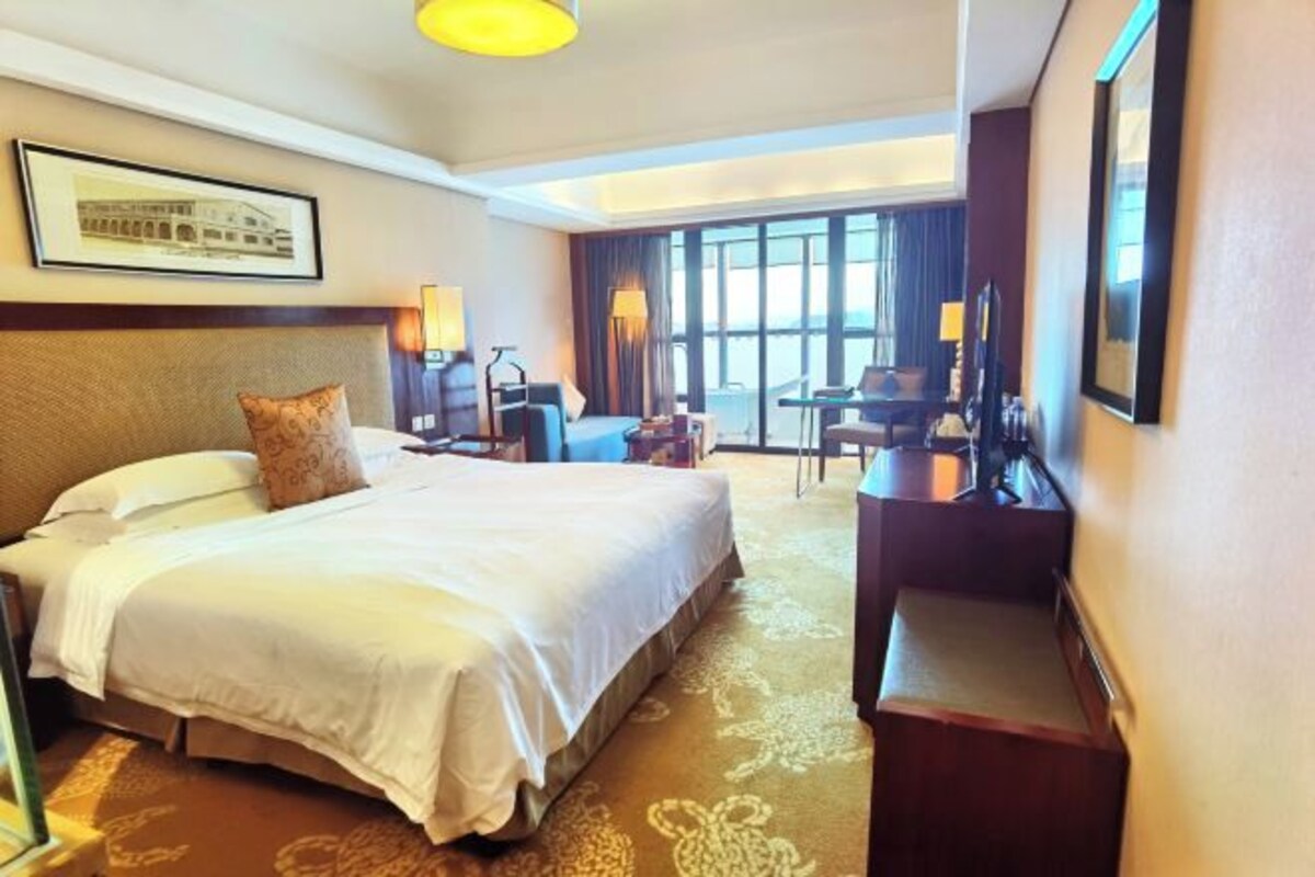 Habitación de hotel con una cama grande, un escritorio, una silla y vista a la ciudad.