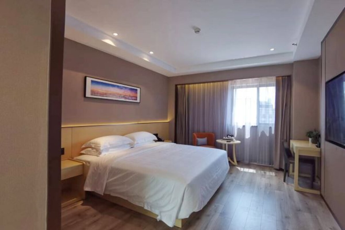 Una habitación de hotel con una cama grande, una mesita de noche, una pequeña mesa y una ventana con cortinas.