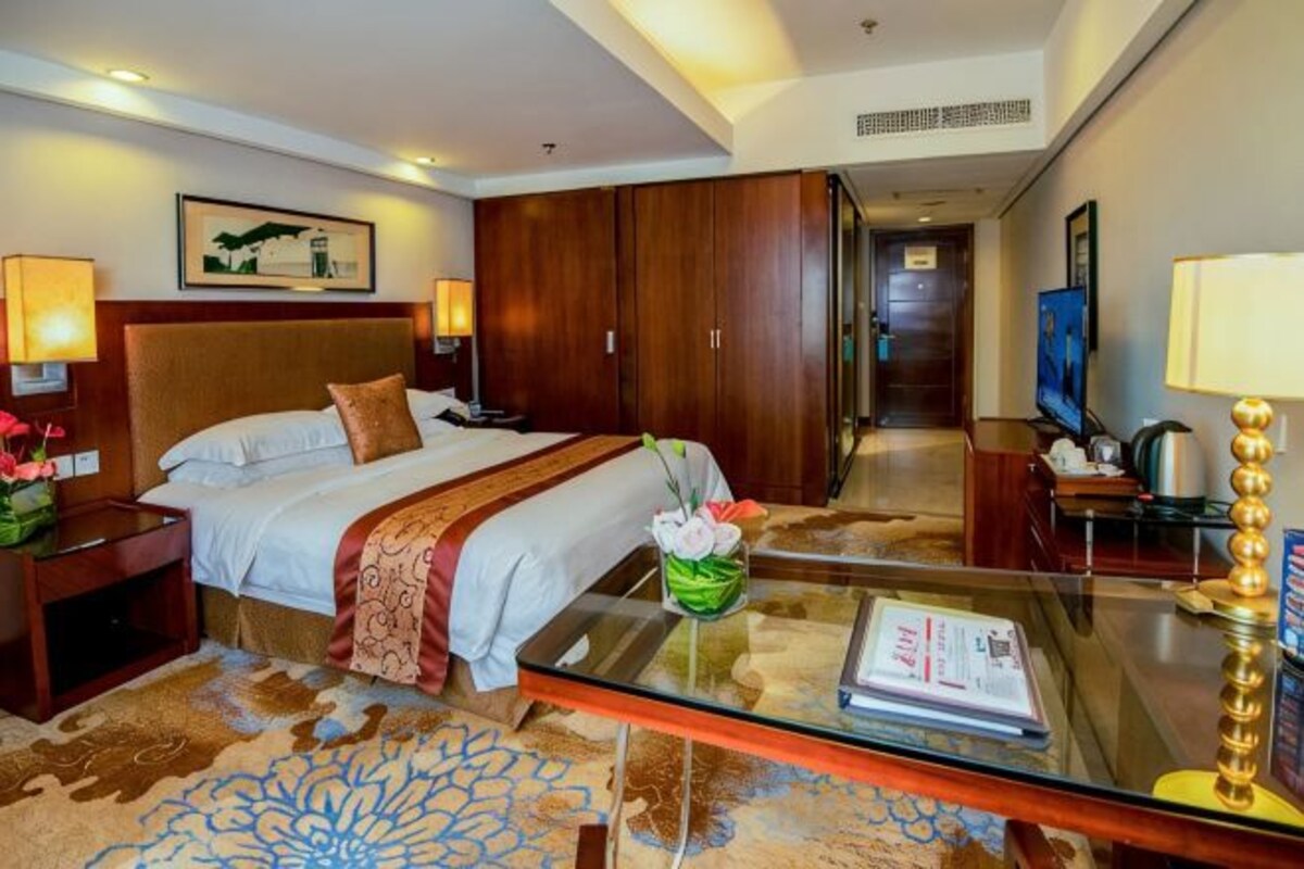 Una habitación de hotel con cama, mesita de noche, lámpara y una mesa de centro de vidrio.