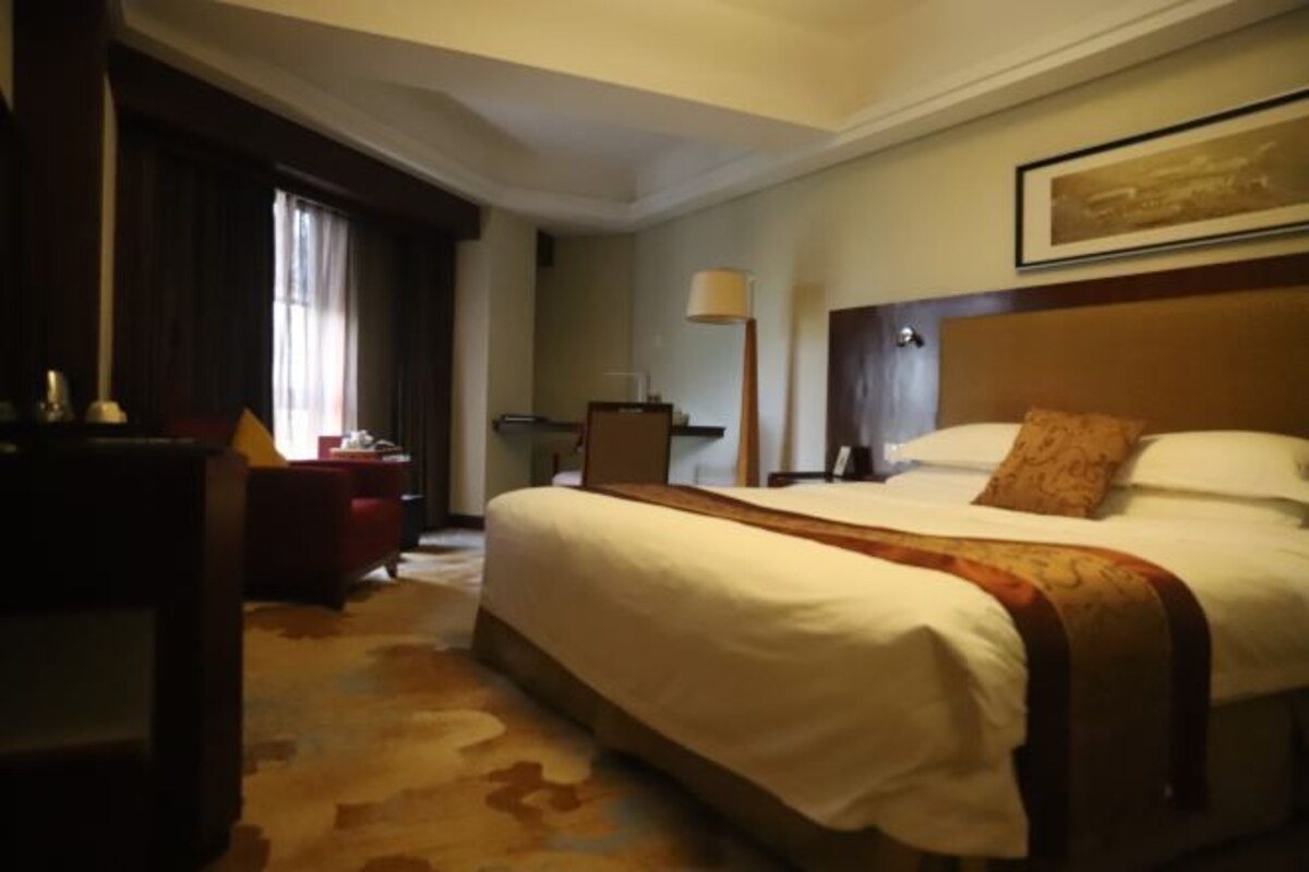 Una habitación de hotel con una cama grande, un escritorio, una silla, una lámpara y un cuadro en la pared.