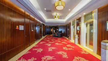A hotel corridor with wooden paneling, a red carpet with gold patterns, and a chandelier.