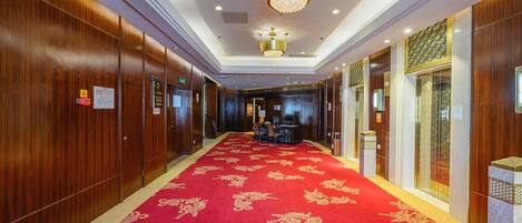 A hotel corridor with wooden paneling, a red carpet with gold patterns, and a chandelier.