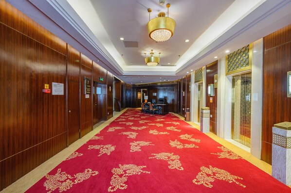 Un pasillo de hotel con paneles de madera, alfombra roja con diseños dorados y un candelabro.