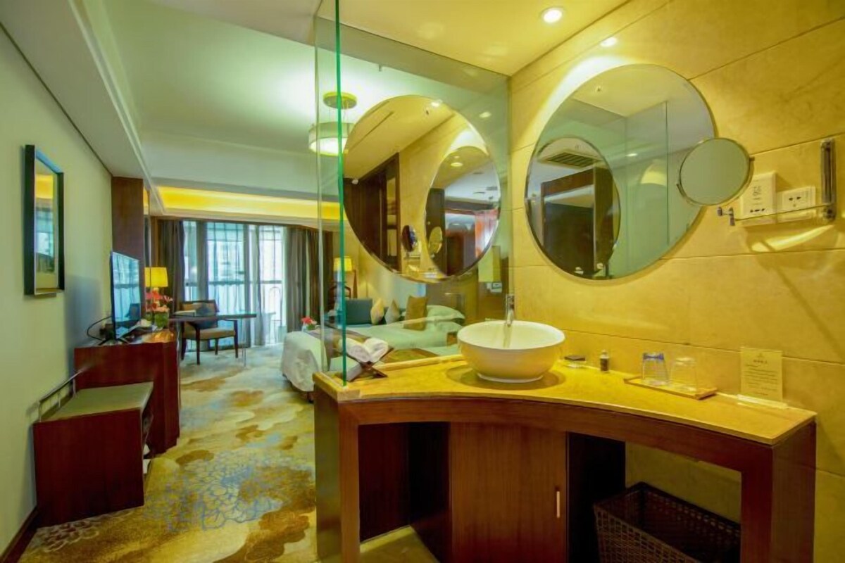 Un baño de hotel con un espejo grande, un lavabo redondo y un tocador de madera.