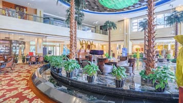 A spacious lobby with a central water feature, seating areas, and a high ceiling with decorative elements.