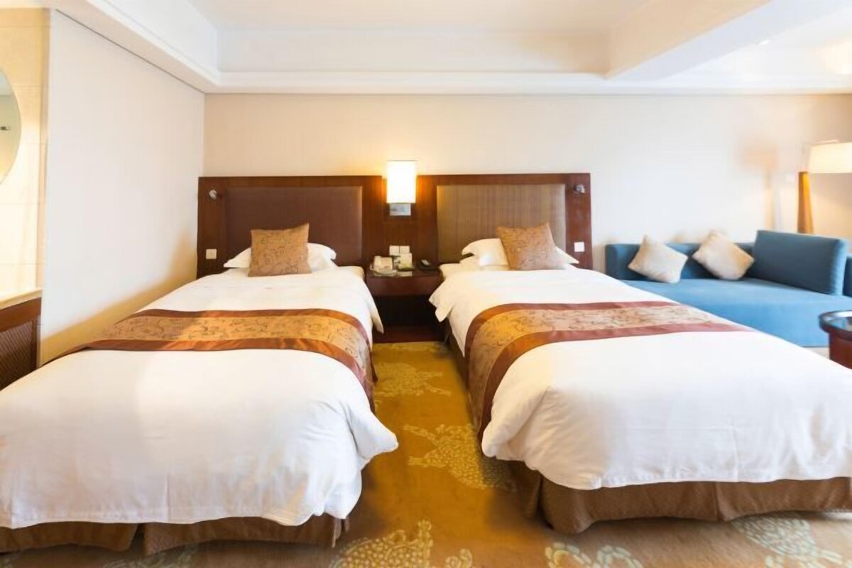 A hotel room with two single beds, a blue sofa, and a nightstand with a lamp.