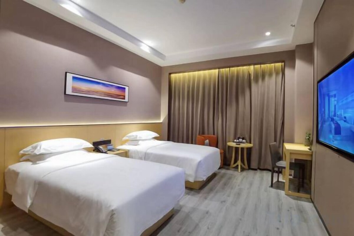 Een hotelkamer met twee bedden, een bureau, een stoel, een televisie en een raam met gordijnen.
