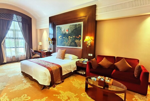 A hotel room with a large bed, a red sofa, a glass coffee table, a desk with a lamp, and a painting on the wall. - Xiamen Zhongwei Gulangwan hotel (Xiamen)
