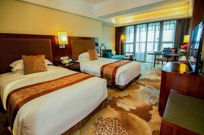 Quarto de hotel com duas camas, uma escrivaninha, uma televisão e uma janela grande.