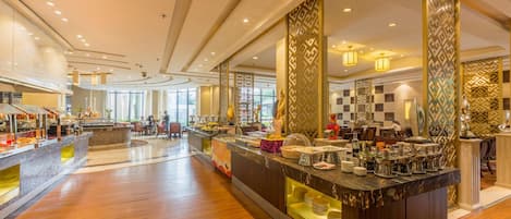A spacious hotel lobby with a central reception desk, seating areas, and a view of the dining area.