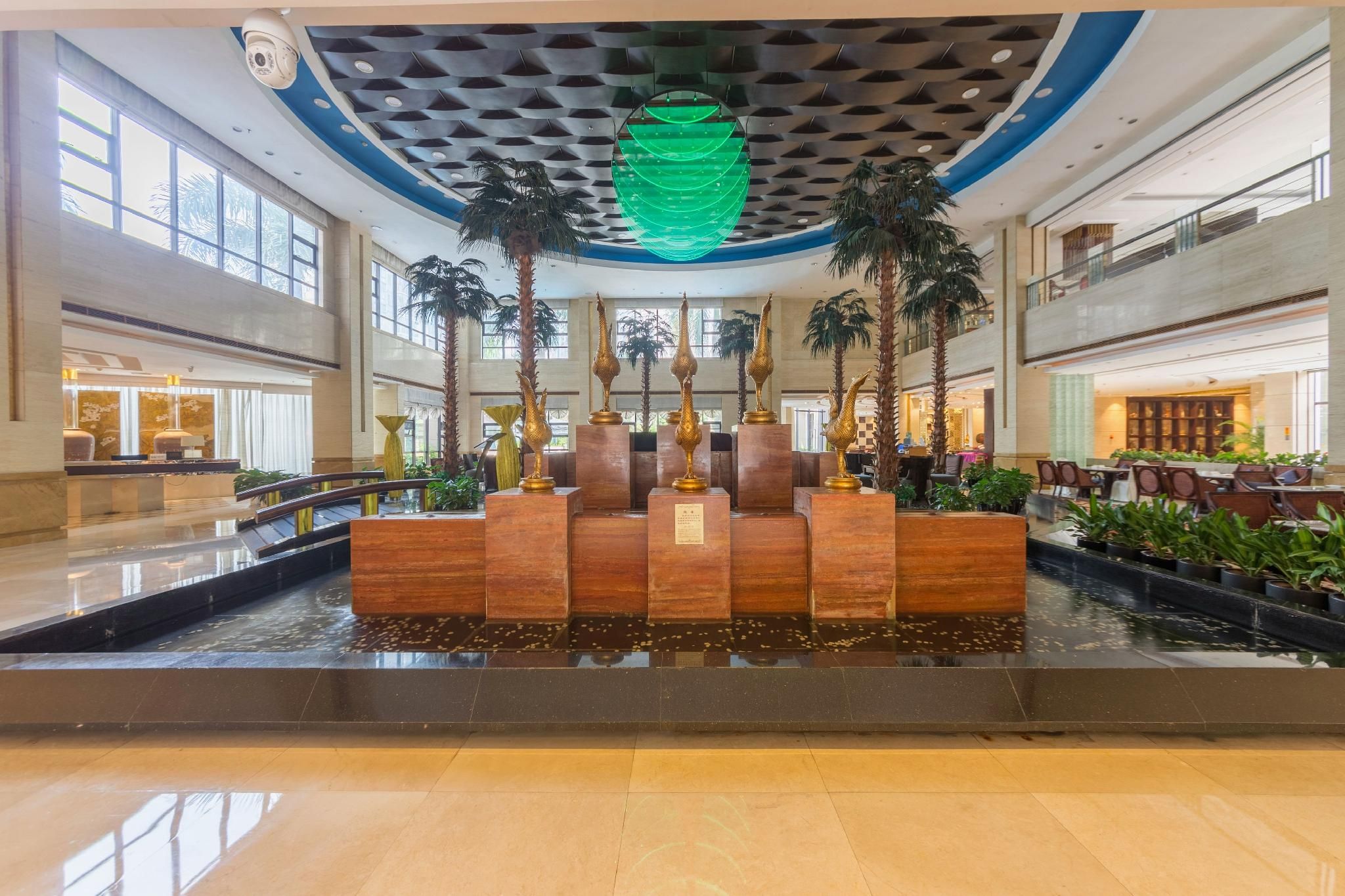 A lobby with a central water feature, palm trees, and a modern ceiling design.