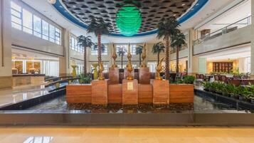 A lobby with a central water feature, palm trees, and a modern ceiling design.