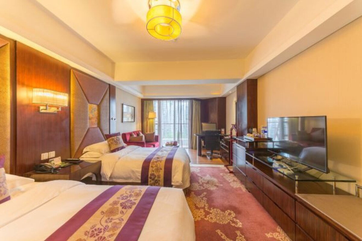 Habitación de hotel con dos camas, televisión, escritorio y un ventanal grande.