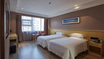 A hotel room with two beds, a desk, a chair, and a window with curtains.