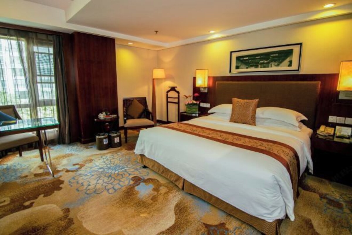 Habitación de hotel con una cama grande, un escritorio, una silla, una lámpara y una ventana con cortinas.