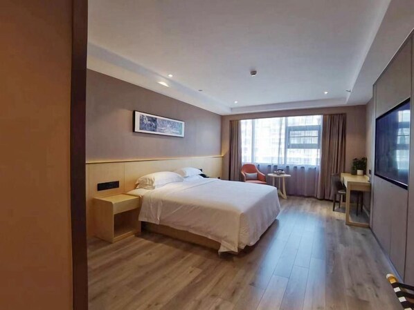 Een hotelkamer met een bed, nachtkastje, stoel, televisie en een raam met gordijnen.