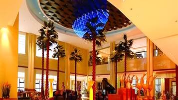 A spacious lobby with a high ceiling, palm trees, and a central staircase.