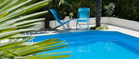 Una piscina con dos sillas reclinables azules y una mesita con un florero.