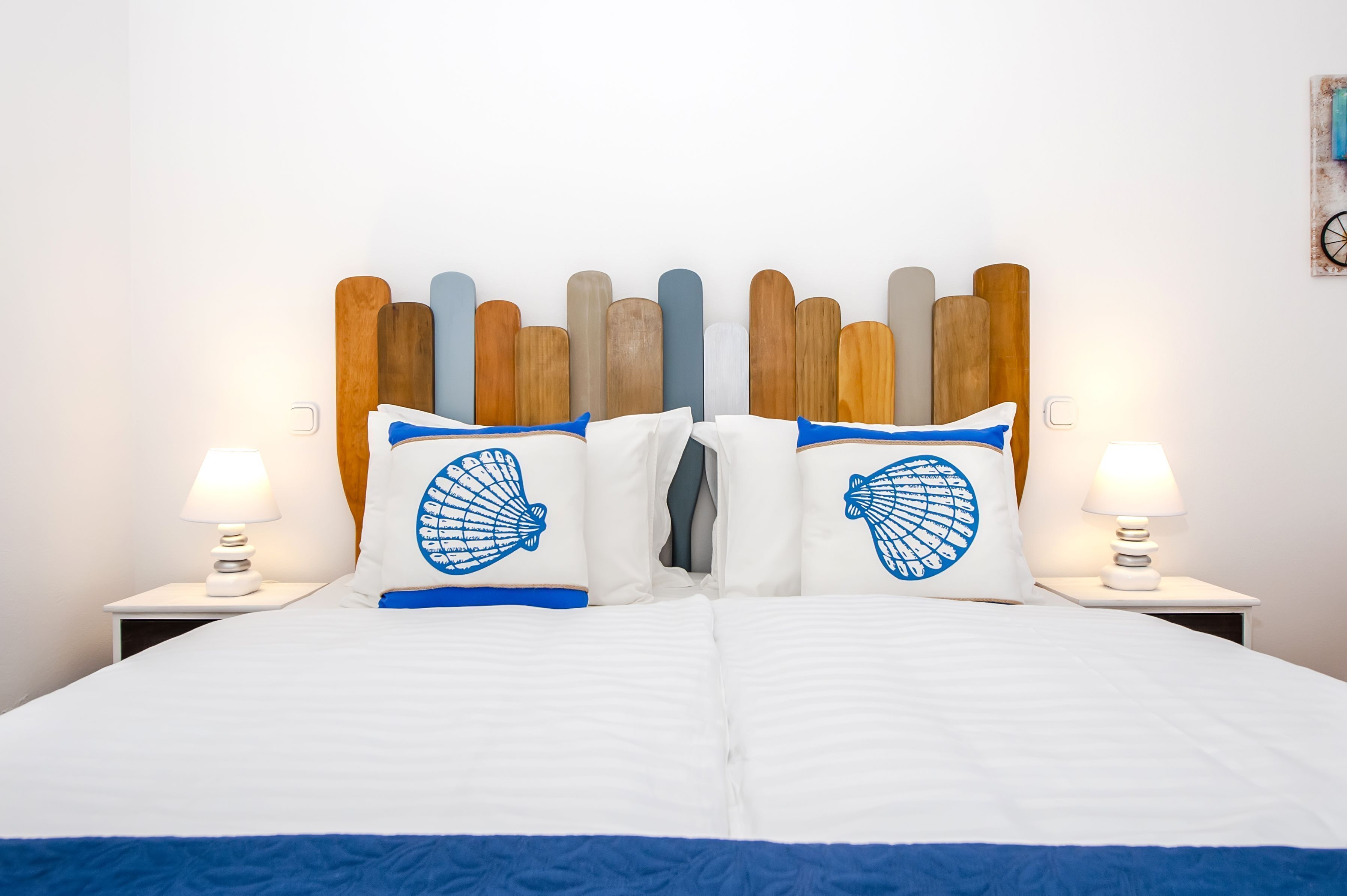 Un lit avec une literie blanche et des touches de bleu, flanqué de deux lampes de chevet.