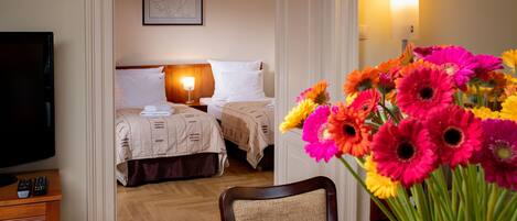 A hotel room with two beds, a TV, a desk with a remote control, and a vase of flowers.