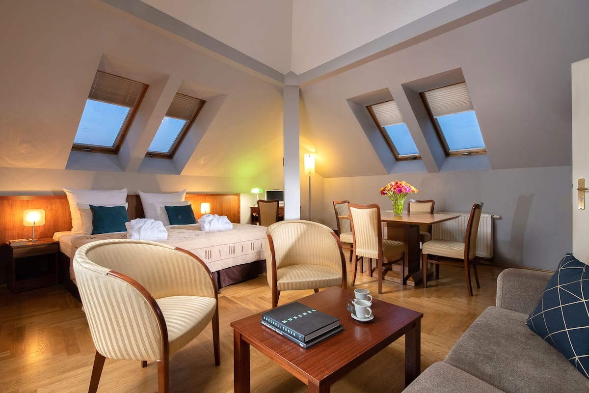A hotel room with a bed, two chairs, a coffee table, a dining table with chairs, and skylights.
