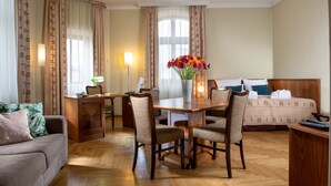 A hotel room with a dining table, chairs, a sofa, a bed, and a vase of flowers.