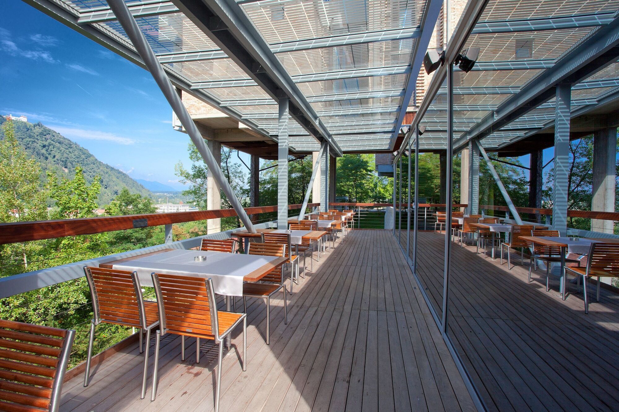 An outdoor dining area with tables and chairs, a wooden deck, and a glass ceiling.