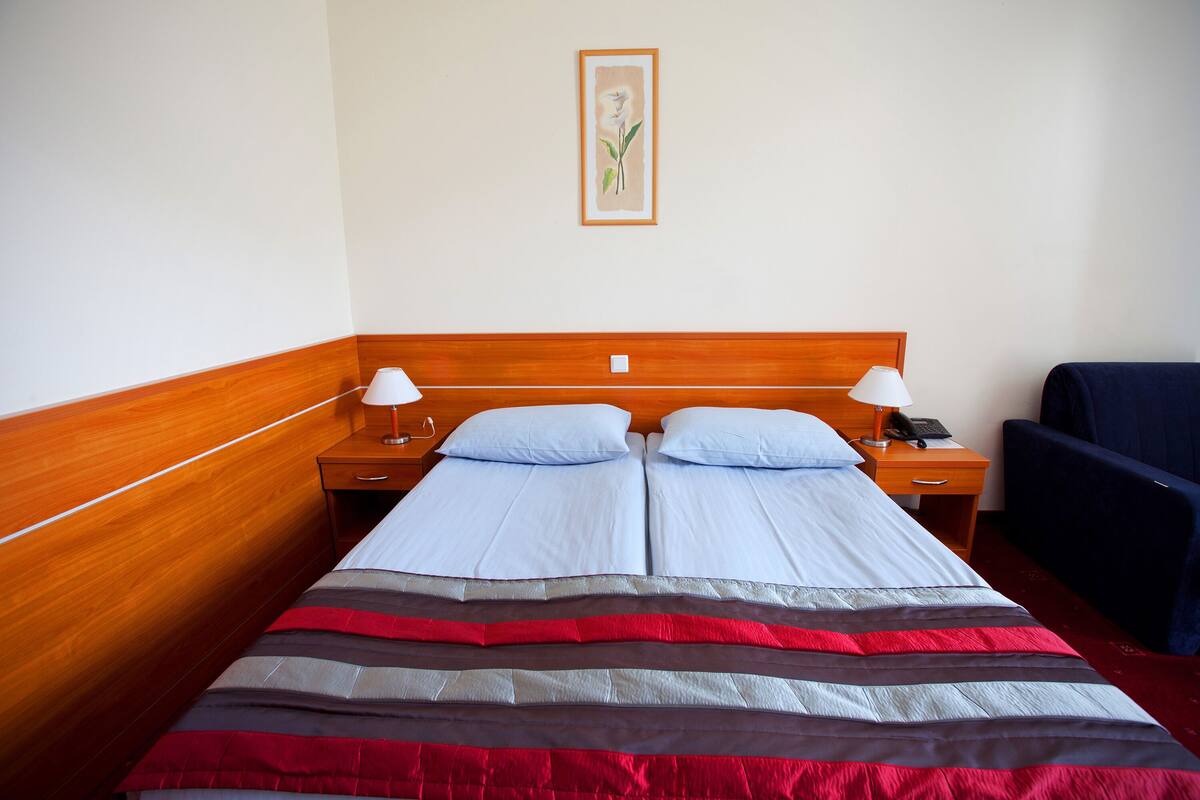 A double bed with a striped bedspread, two bedside tables with lamps, a wooden headboard, and a framed picture on the wall.