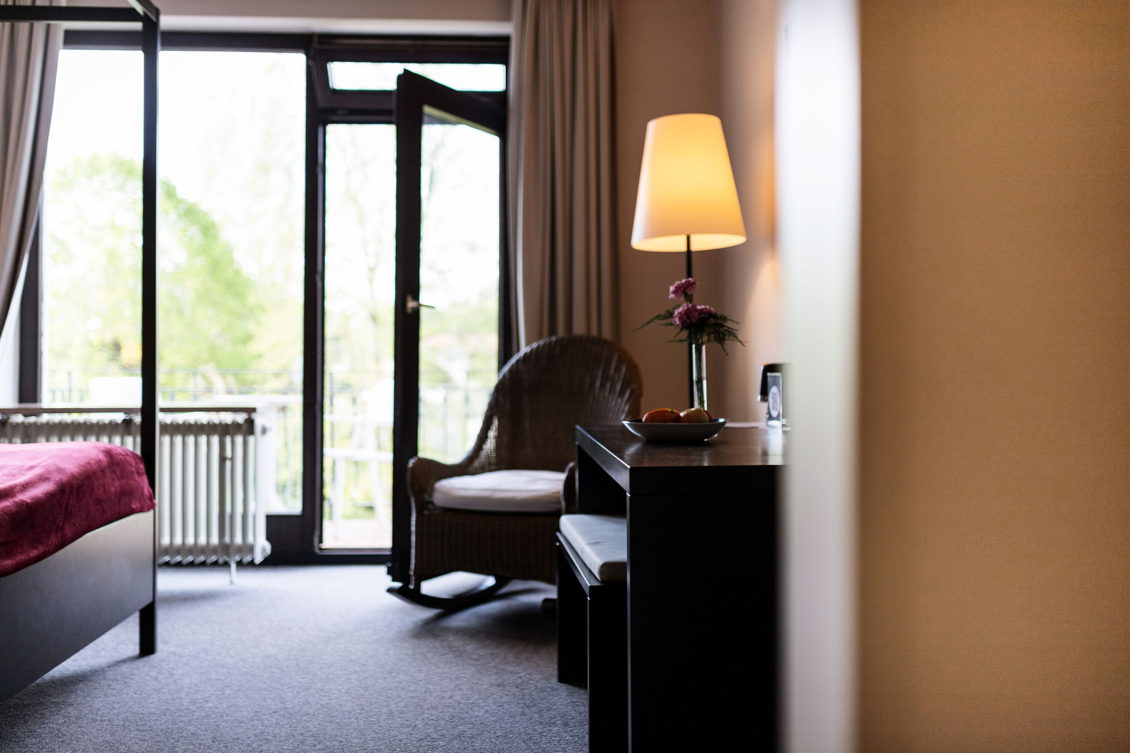 Una habitación de hotel con cama, una silla, un escritorio con lámpara y vistas al exterior.