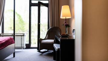 Ein Hotelzimmer mit einem Bett, einem Sessel, einem Schreibtisch mit Lampe und Blick ins Freie.